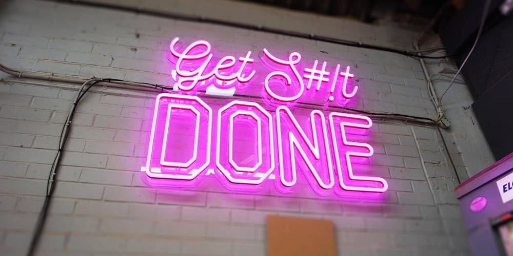 Неоновая надпись Get S#!t Done на кирпичной стене офиса
