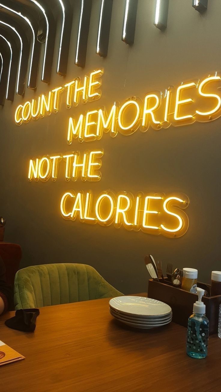 Неоновая надпись Count The Memories Not The Calories жёлтым неоном над столиком в ресторане