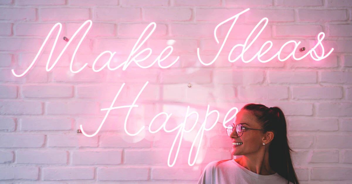 Девушка на фоне розовой неоновой надписи Make Ideas Happen в салоне