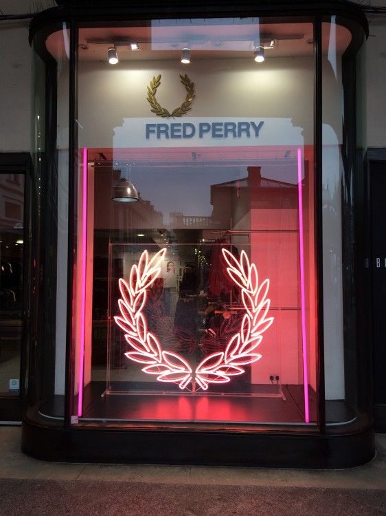 Неоновый логотип Fred Perry розовым неоном в витрине магазина одежды на улице