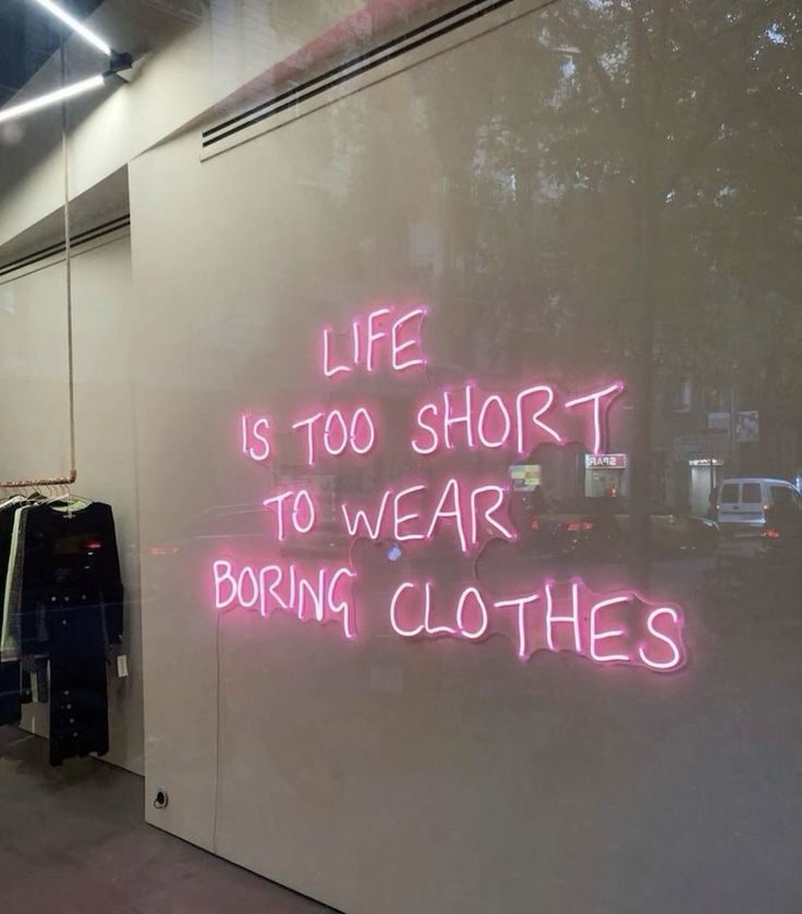 Неоновая надпись Life is too short to wear boring clothes розовым неоном в витрине магазина одежды