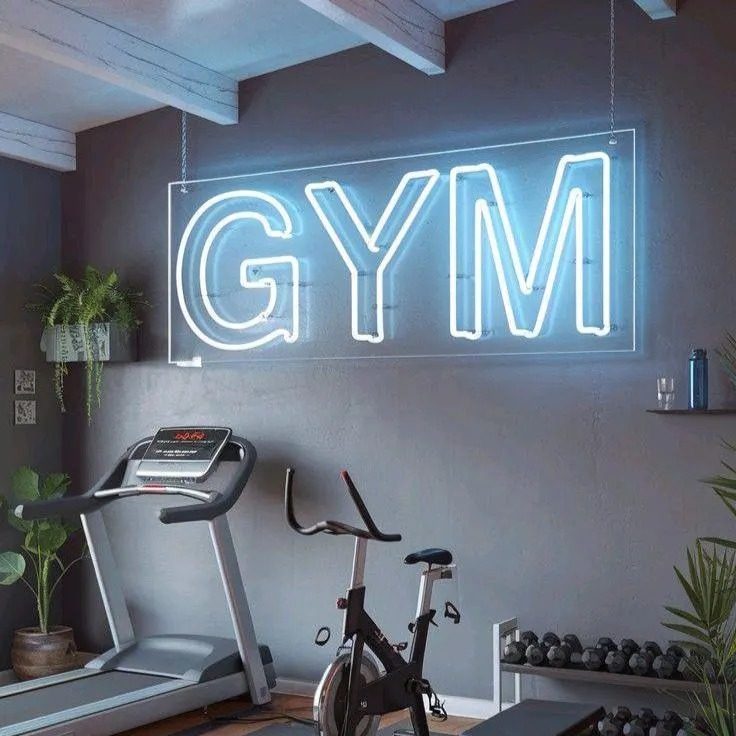 Неоновая надпись GYM синим неоном над тренажёрами в зале