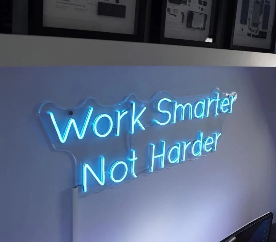 Неоновая надпись Work Smarter Not Harder в офисе на светлой стене