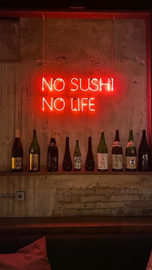 Неоновая надпись No Sushi No Life красным неоном над полкой с бутылками саке