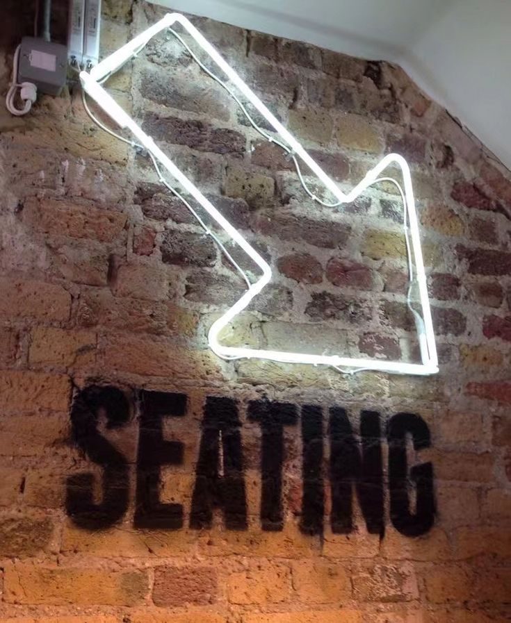 Неоновая стрелка белым неоном на кирпичной стене с надписью Seating — навигация в магазине