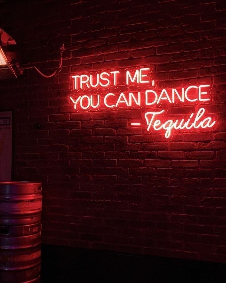 Неоновая надпись Trust Me You Can Dance Tequila красным неоном на кирпичной стене бара