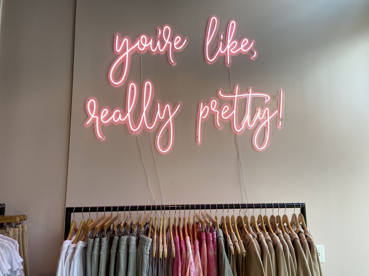 Неоновая надпись You're like really pretty розовым неоном над вешалкой с одеждой в магазине
