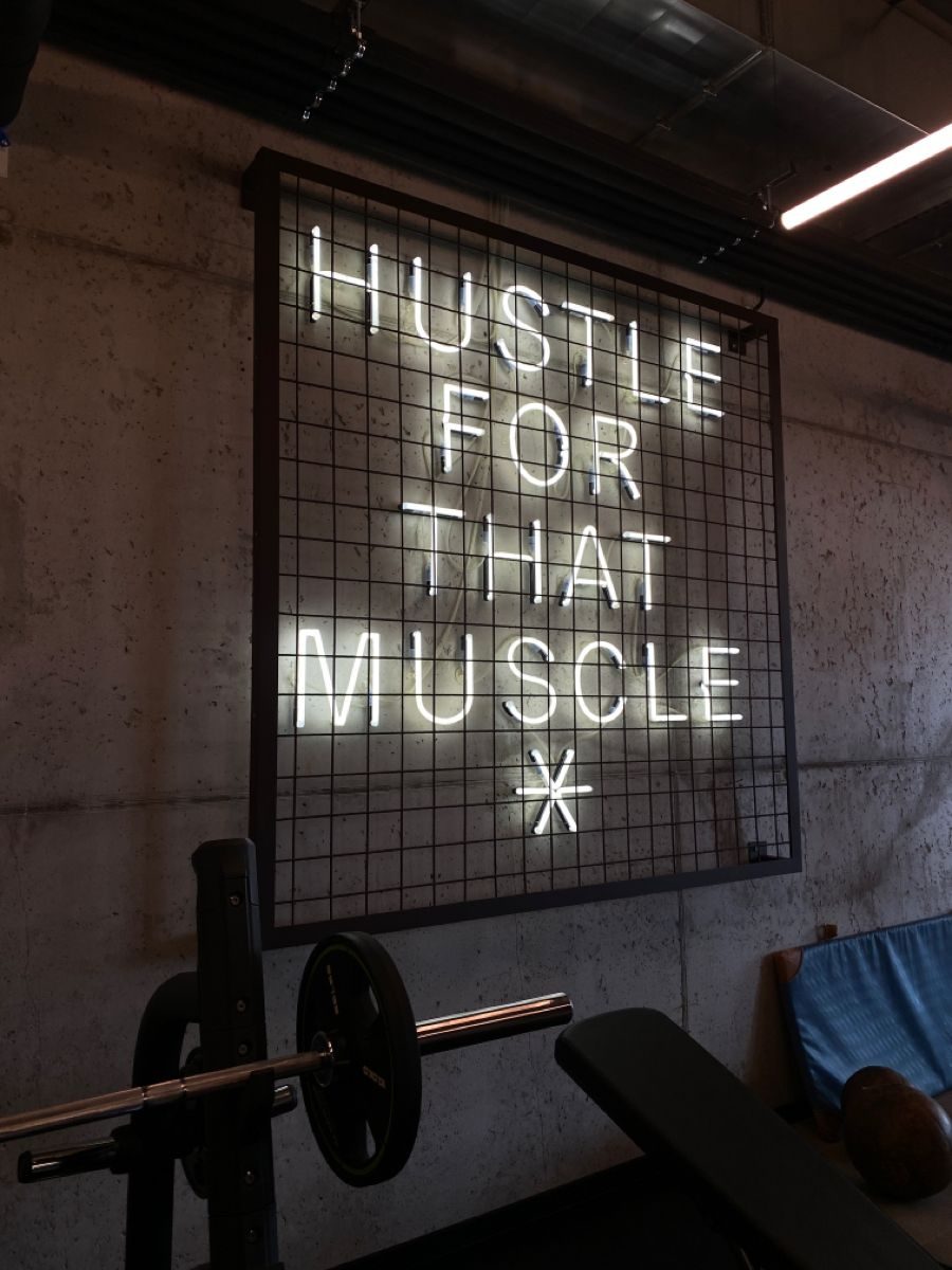 Неоновая надпись Hustle For That Muscle на металлической сетке в фитнес-зале