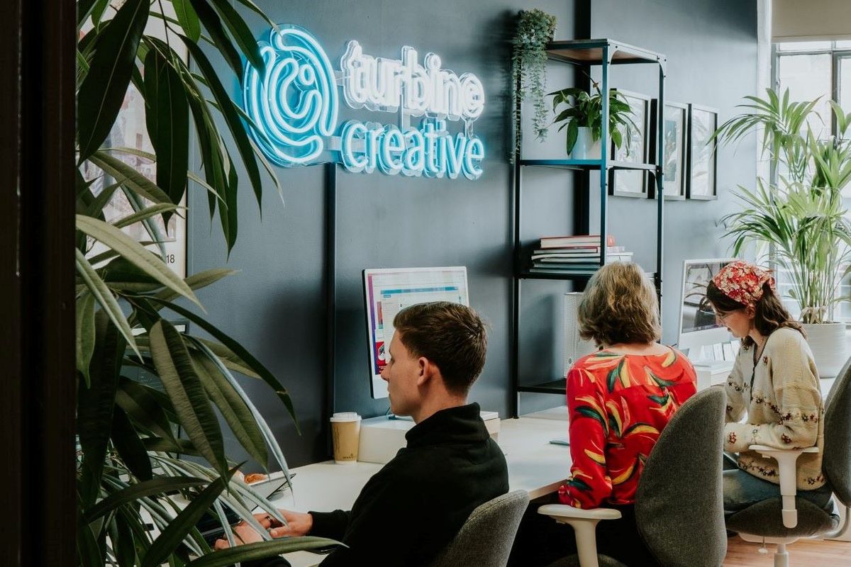 Неоновый логотип Turbine Creative над рабочими местами в современном офисе
