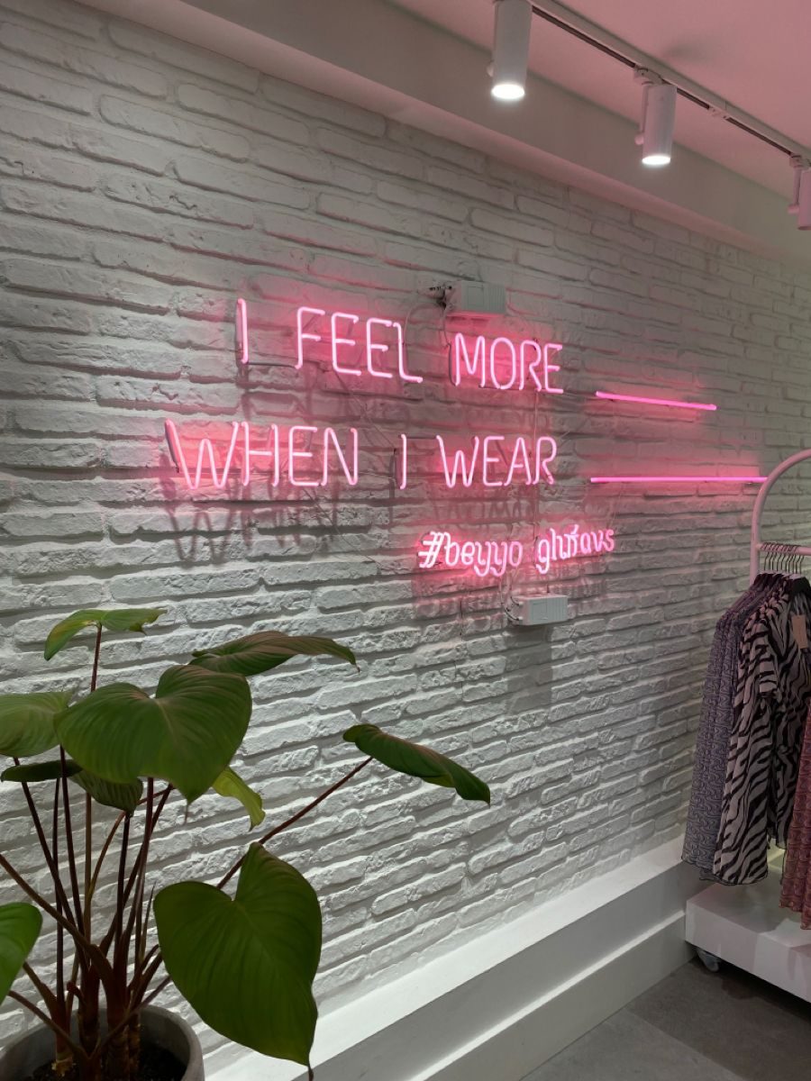Неоновая надпись I Feel More When I Wear розовым неоном на белой кирпичной стене в магазине одежды