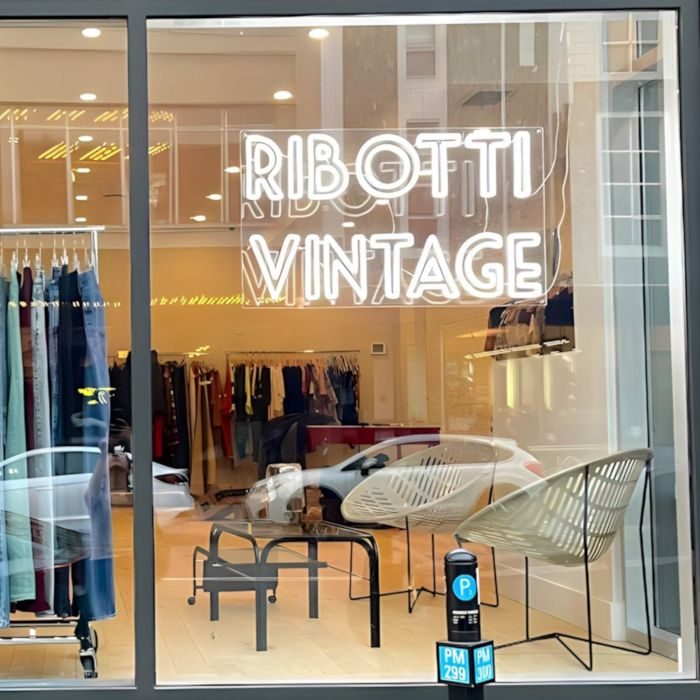 Неоновый логотип Ribotti Vintage белым неоном в витрине магазина одежды на улице