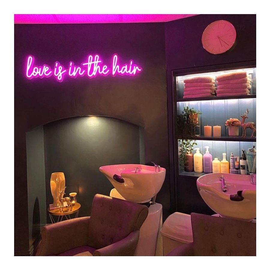 Неоновая надпись love is in the hair в интерьере парикмахерской с розовыми раковинами