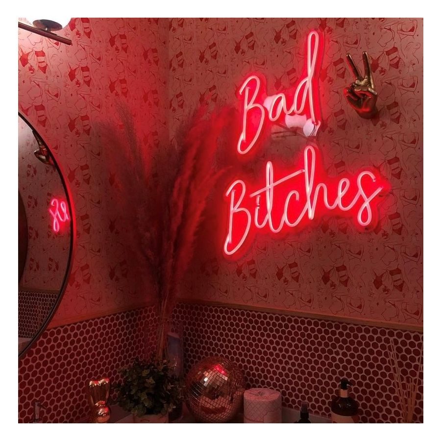 Неоновая надпись Bad Bitches красным неоном на декорированной стене в салоне