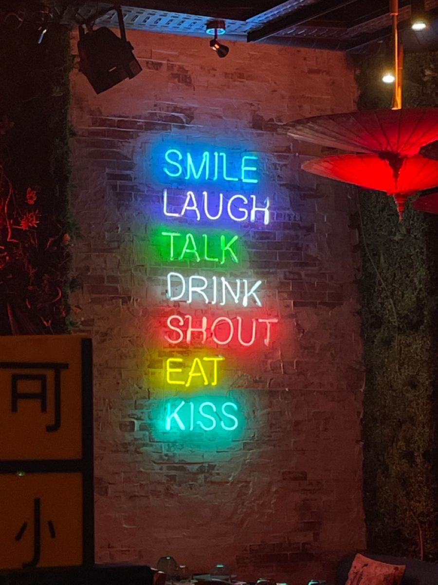 Разноцветная неоновая надпись Smile Laugh Talk Drink Shout Eat Kiss на кирпичной стене